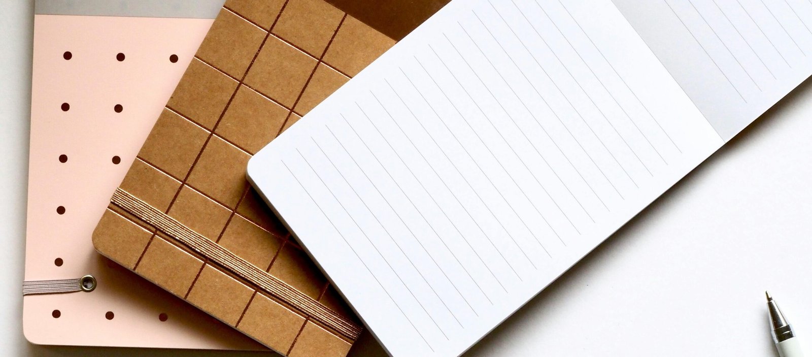 A minimalist flat lay featuring stylish notebooks and pens on a white background.